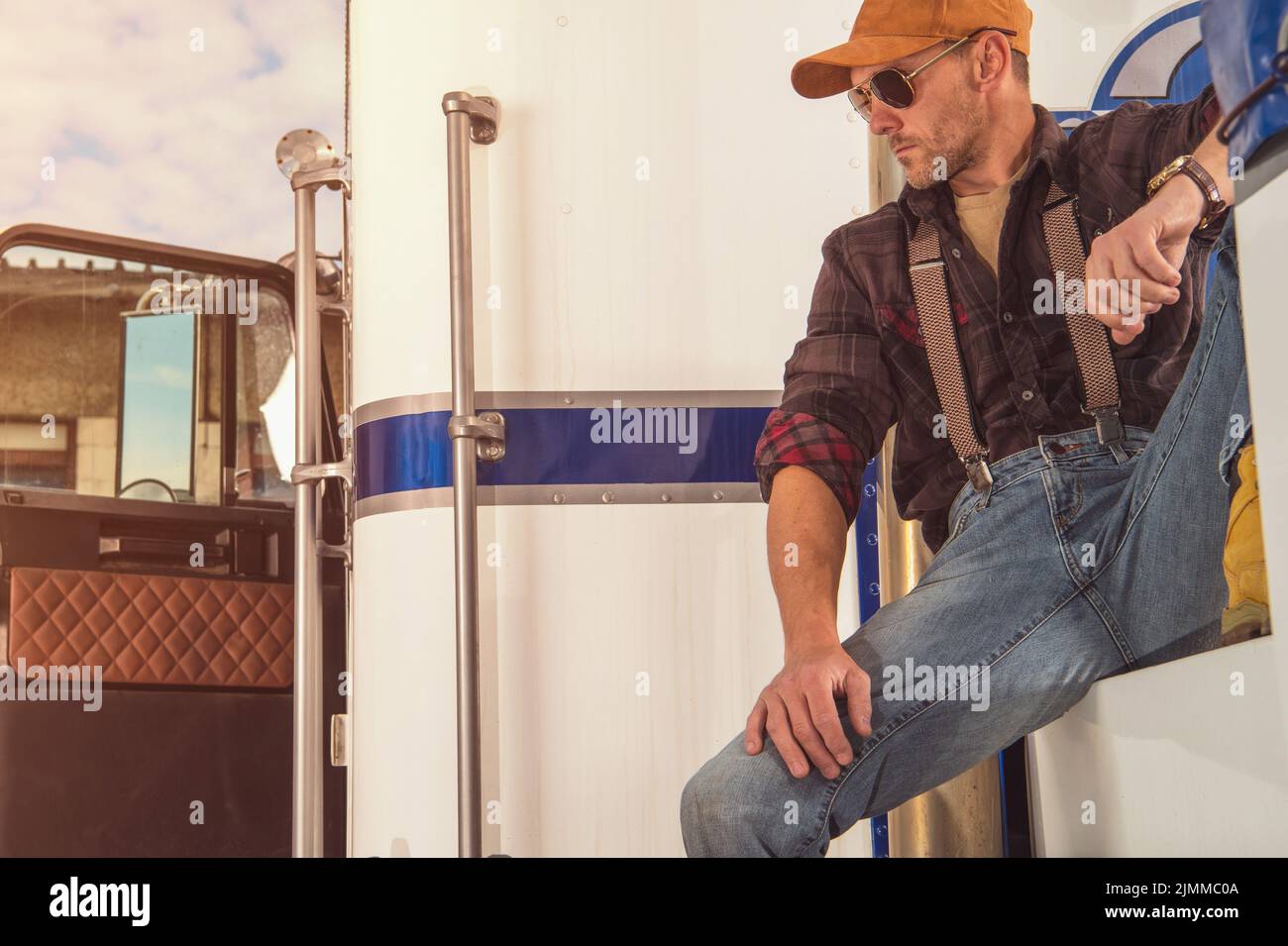 Exhausted Caucasian Middle Aged Truck Driver Sitting Outside His Lorry Taking a Relaxing Break After Challenging Route. Transportation Industry Theme. Stock Photo