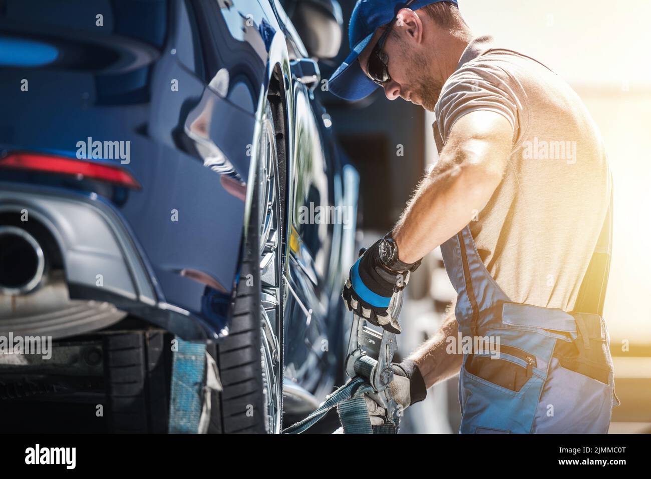 Caucasian Towing Worker Fastening Broken Vehicle with Tie Down Straps. Professional Roadside Assistance and Breakdown Coverage Services. Automotive an Stock Photo