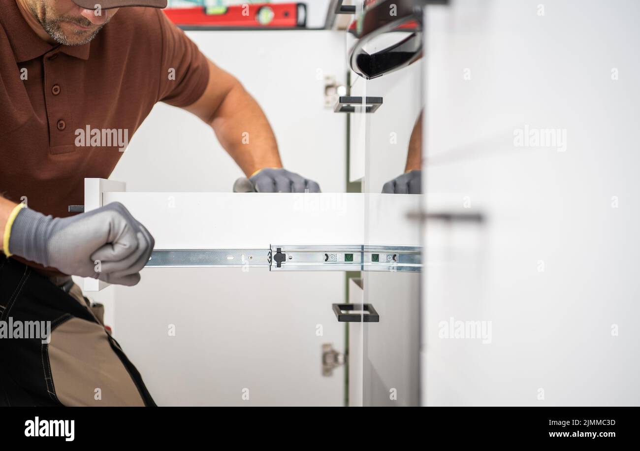 Caucasian Household Worker Assembling Drawer Slide Element to Install Roll-Out Shelf in the Cabinet. Kitchen Renovation and Furnishing Theme. Stock Photo