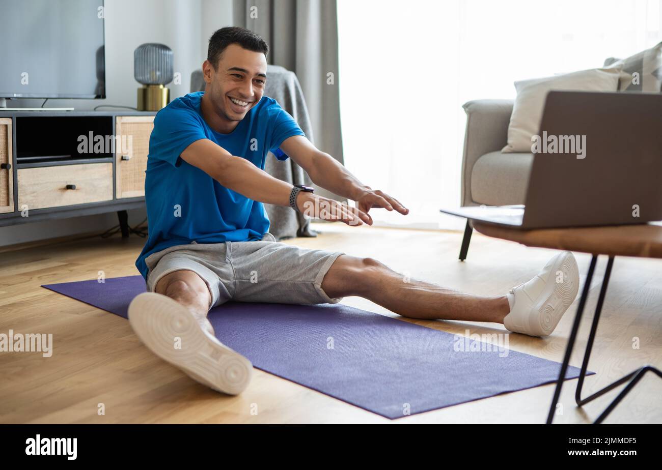 Domestic workout. Active arab man doing stretching exercises while