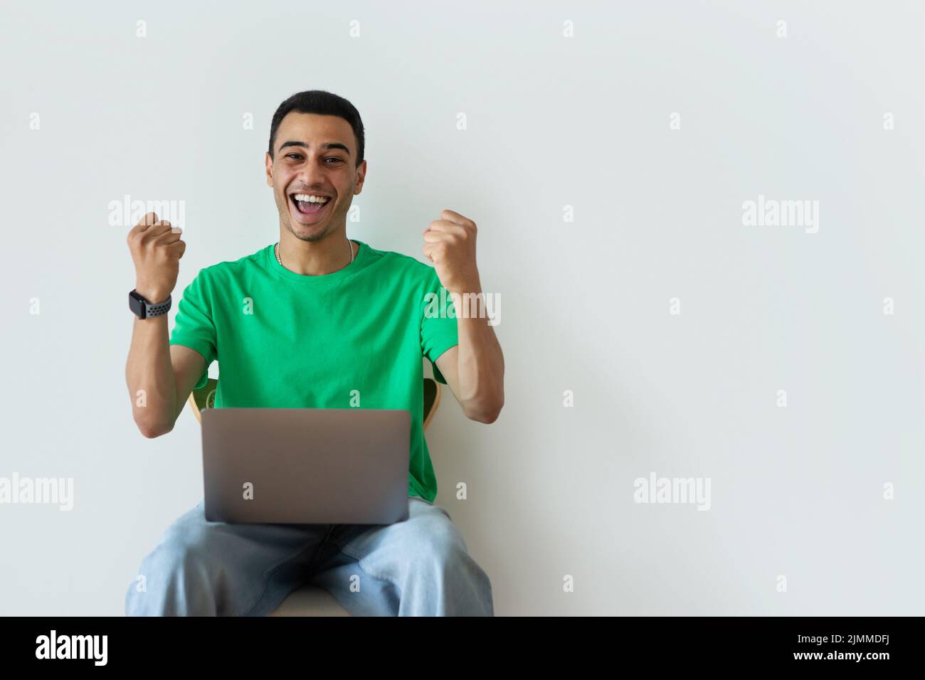 Overjoyed arab guy making YES gesture, sitting on chair with laptop