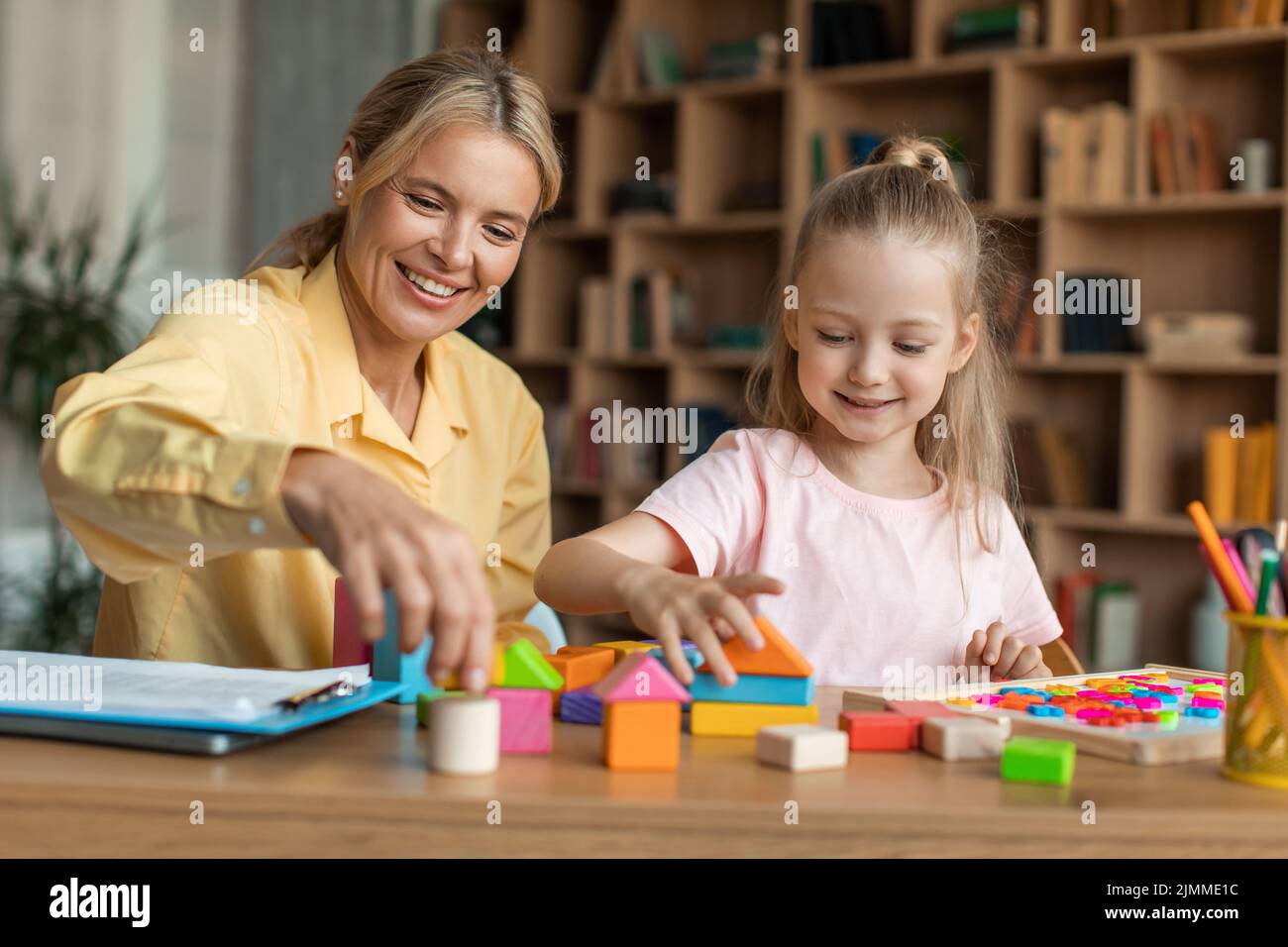 Games and education concept. Positive female teacher exercising with smart girl, playing wooden development blocks Stock Photo