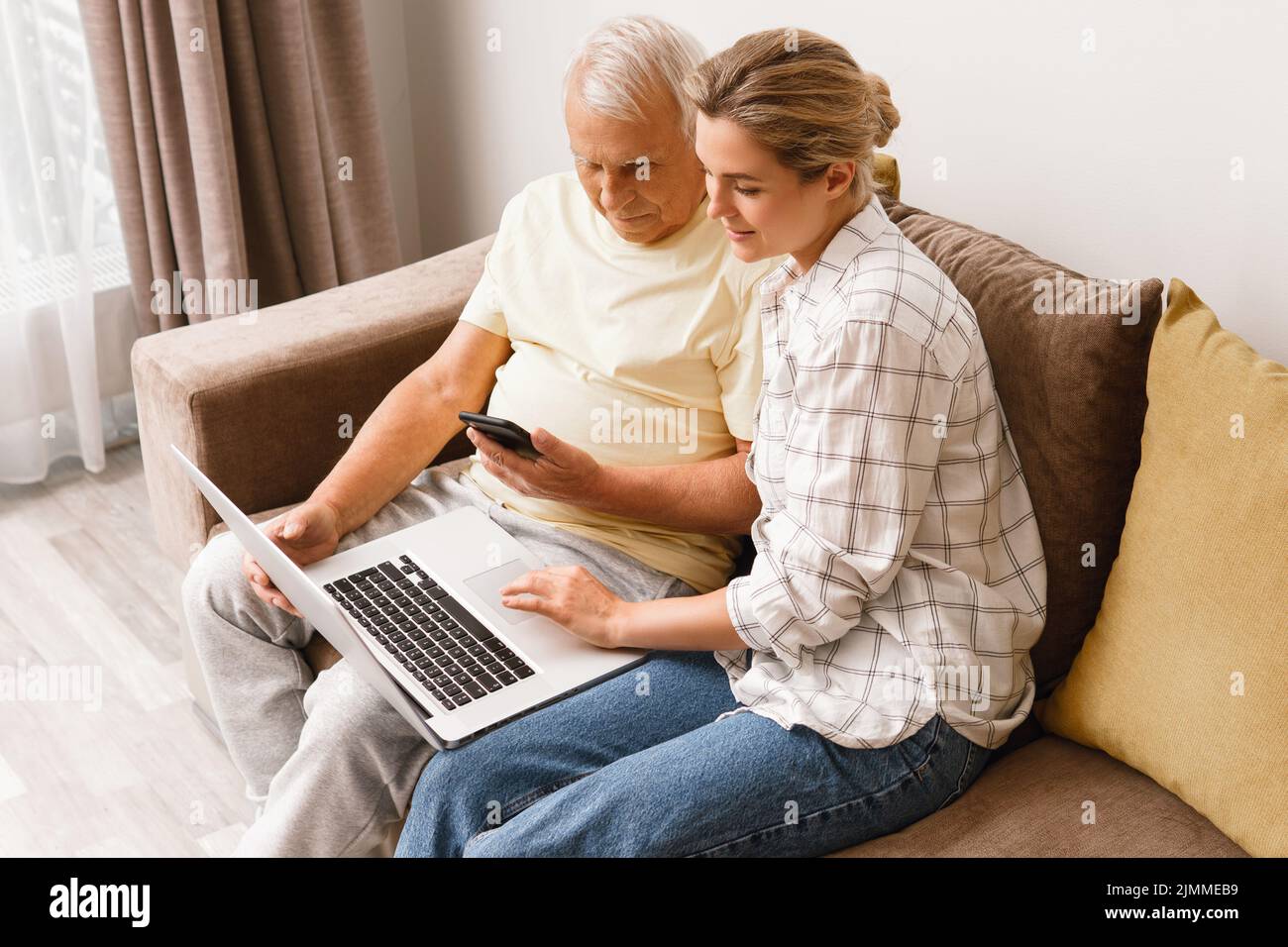 Woman explaining to elderly man how to use laptop and smatphone Stock Photo