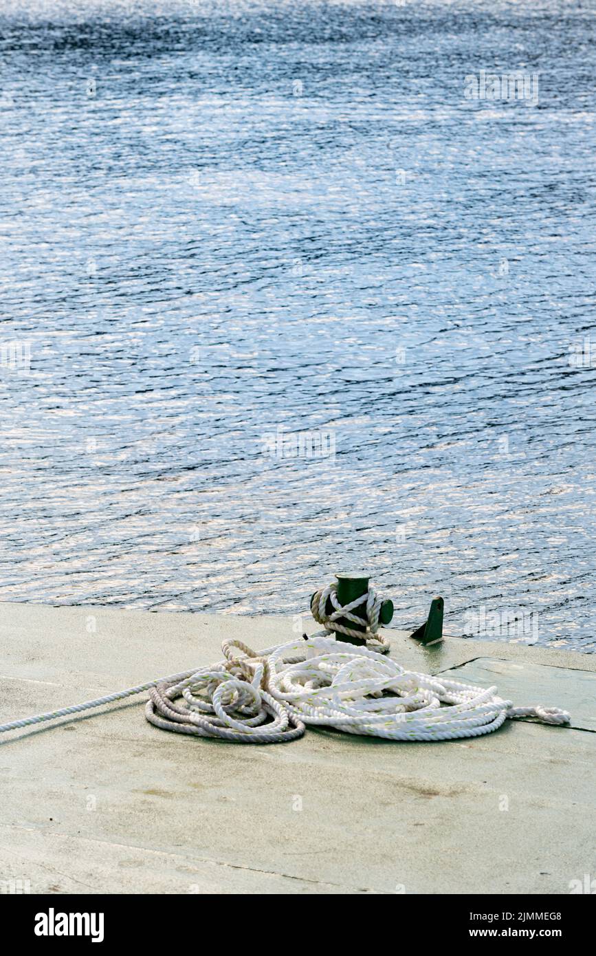 A wharf bollard, dock cleat or boat cleat in the sun with heavy nylon mooring lines attached in Australia Stock Photo
