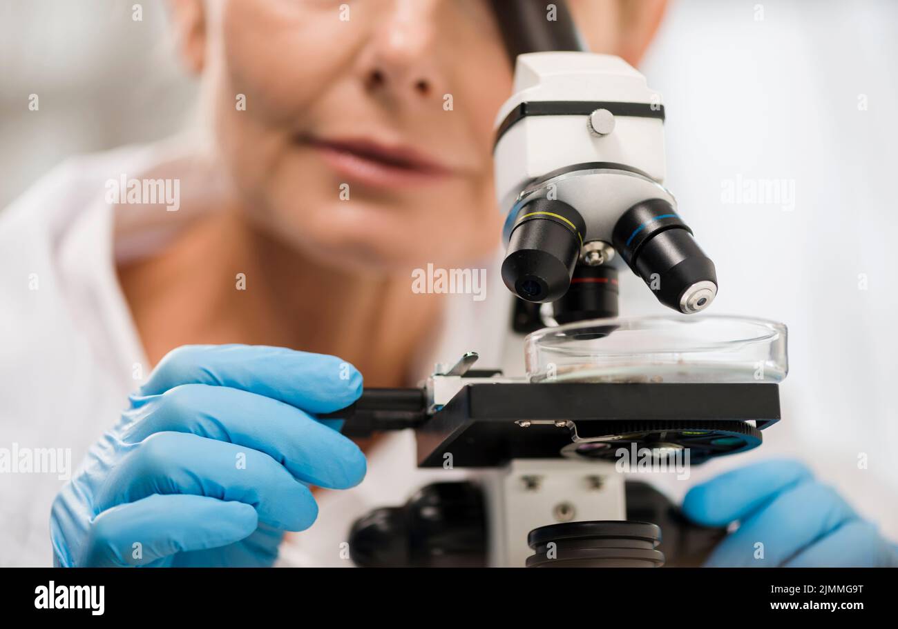 Defocused female scientist looking through microscope Stock Photo