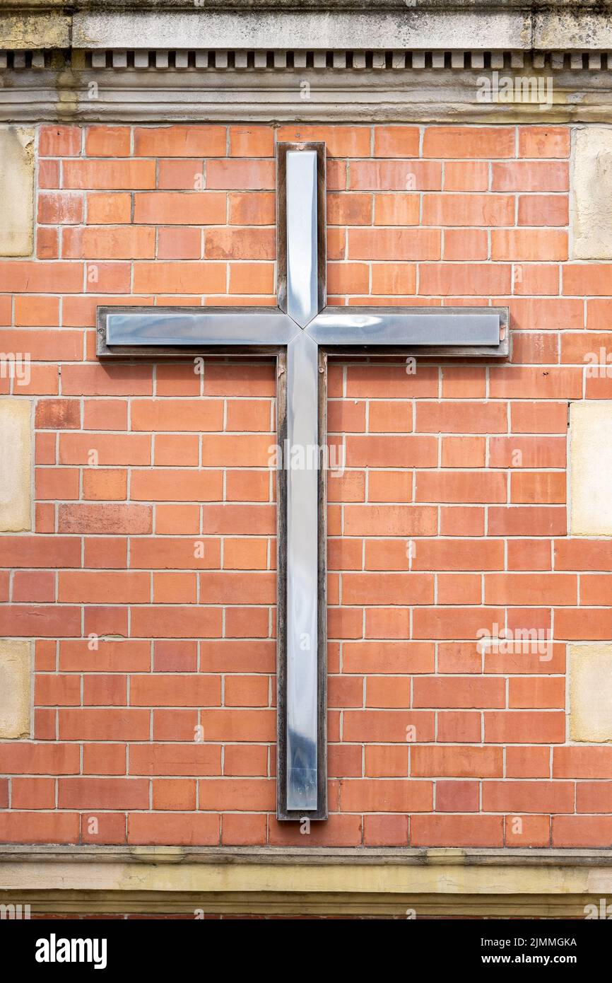 Shiny metal cross mounted on red brick wall of modern church Stock
