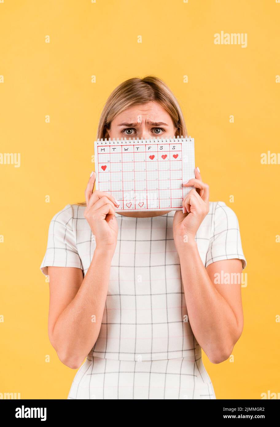 Shocked woman covering her face with period calendar Stock Photo