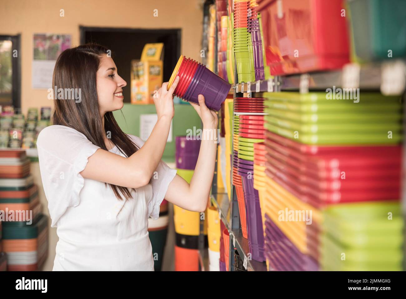 Happy woman arranging colorful flowering plants shelf Stock Photo