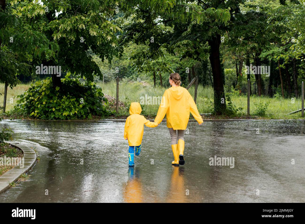 Long shot mother son holding hands while wearing rain coats Stock Photo