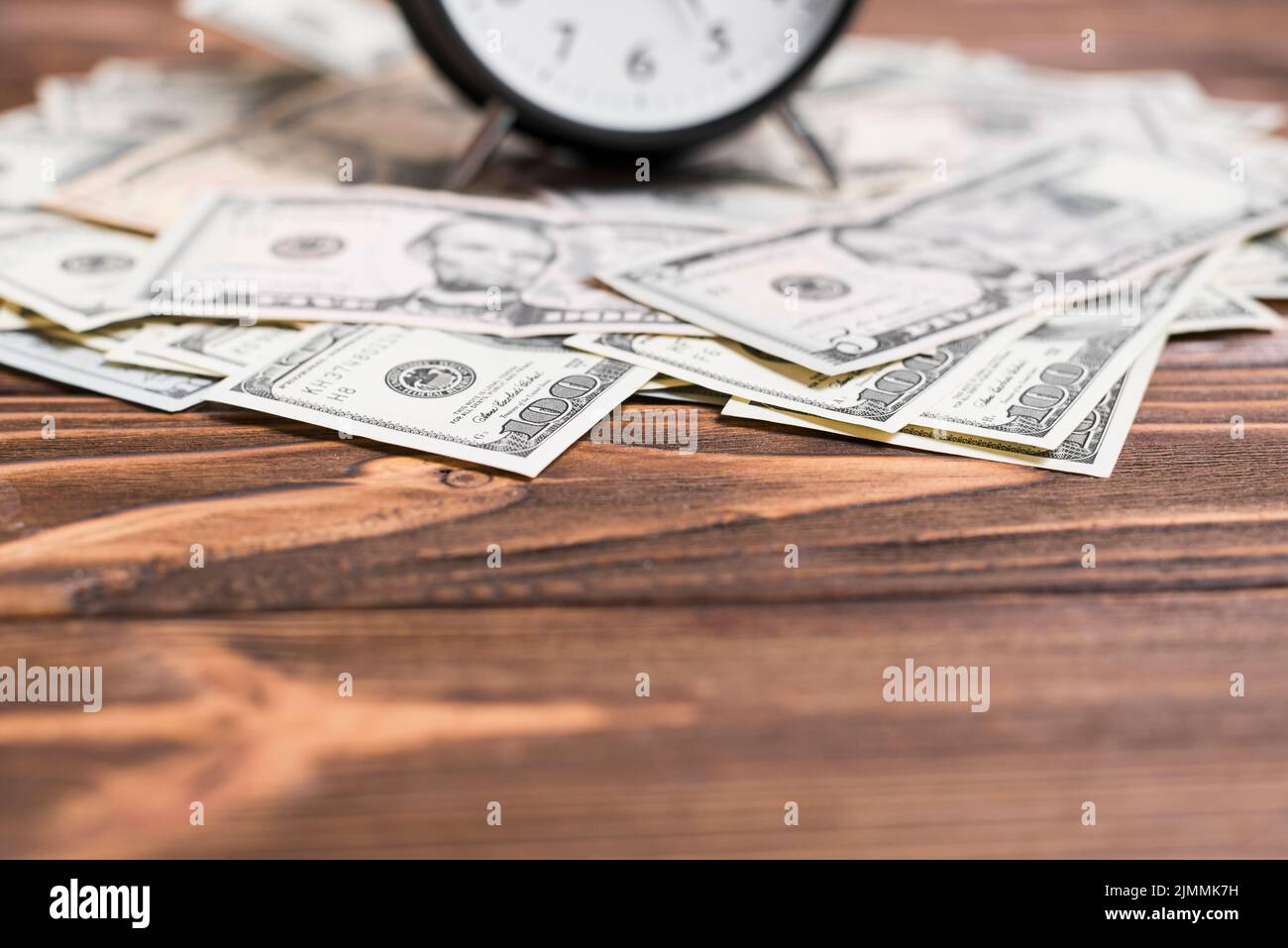 Close up alarm clock us dollar currency notes wooden desk Stock Photo