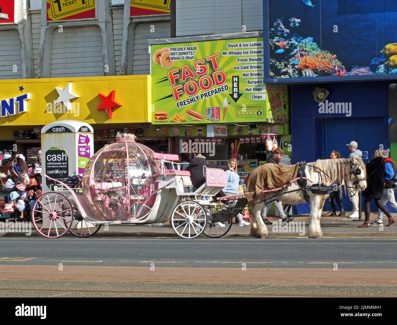 People walking past a coach and horse on the golden mile in blackpool outside the sealife centre food stalls and amusement arcad Stock Photo