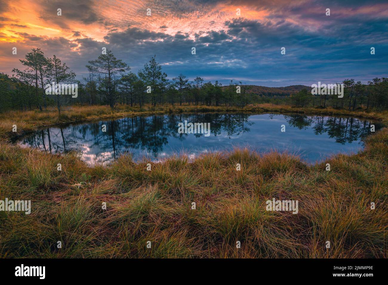 Beautiful autumn landscape and small lake in the swamp. Fantastic sunrise lights and colorful clouds reflection on the water in the bog, Tinovul Mohos Stock Photo