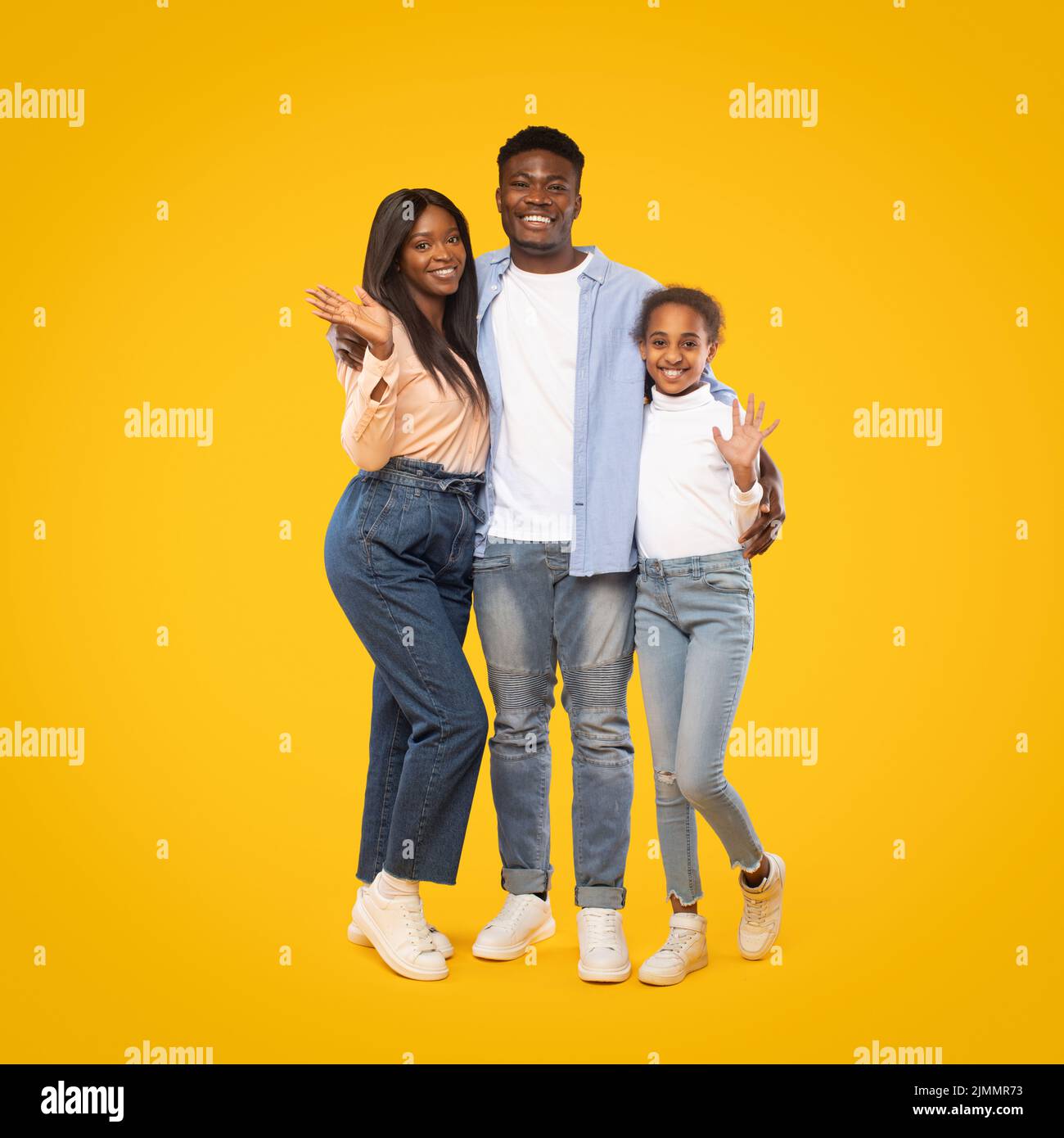 Portrait of happy african american family of man, woman and girl waving hands while posing over yellow background Stock Photo