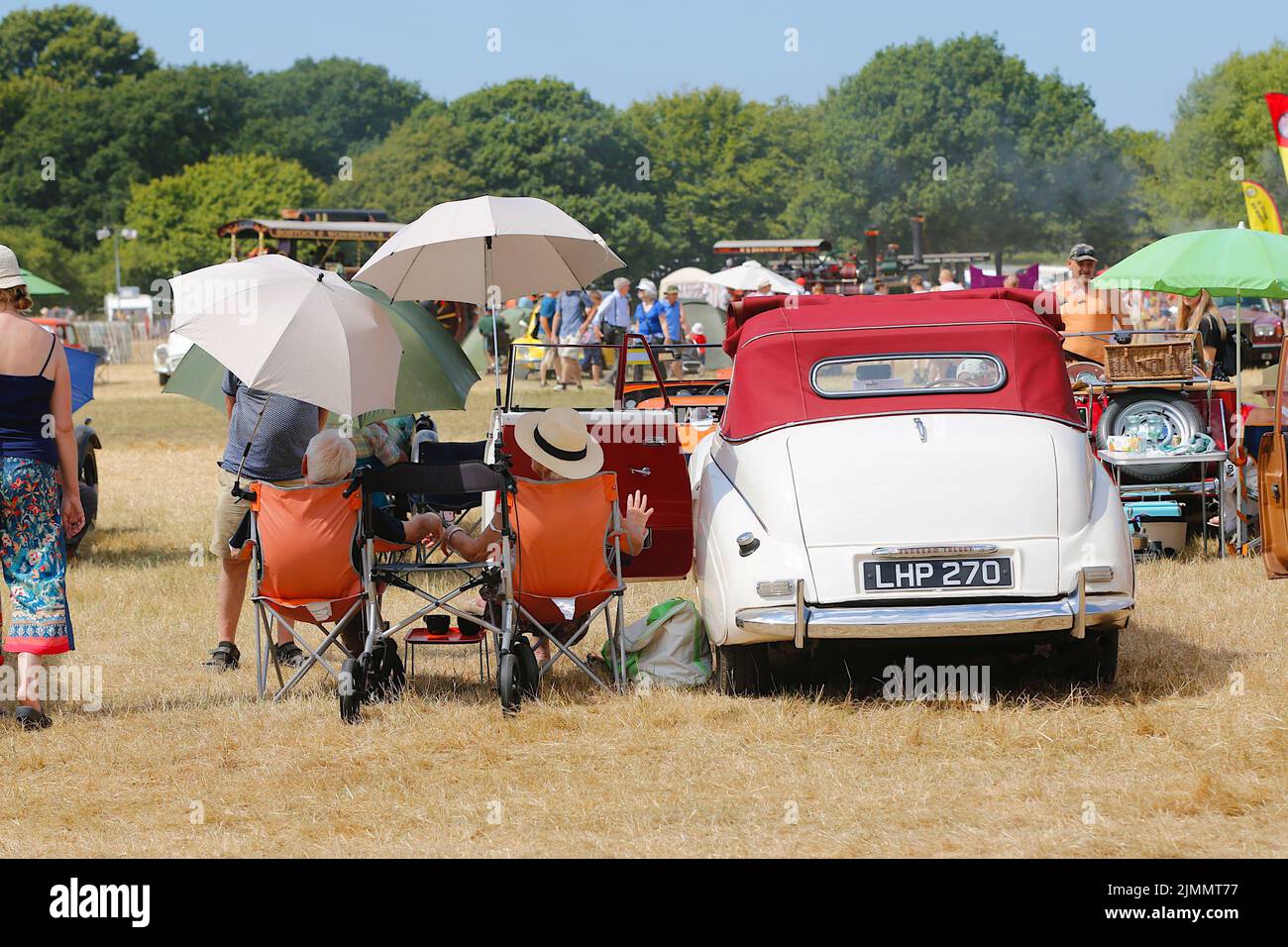 Woodchurch, Kent, UK. 07 August, 2022. On a hot and sunny day in the Kent countryside thousands of people arrive at one of the largest steam rally events in the south east. An elderly couple relax under sunshade by their Sunbeam Talbot. Photo Credit: Paul Lawrenson/Alamy Live News Stock Photo
