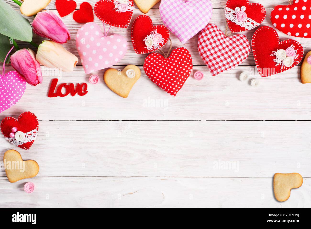 Handmade sewed Valentine fabric hearts with tulips and cookies flat lay background on white wooden table Stock Photo