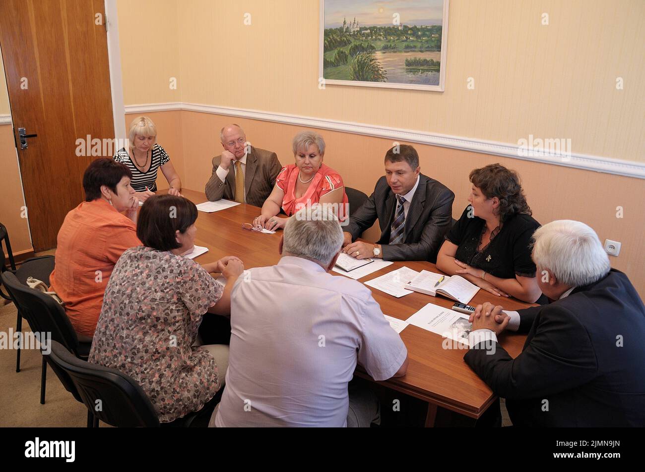 Middle aged men and women teachers sitting at the table in the office and communicating. Typical meeting in the teacher's room of the Ukrainian second Stock Photo