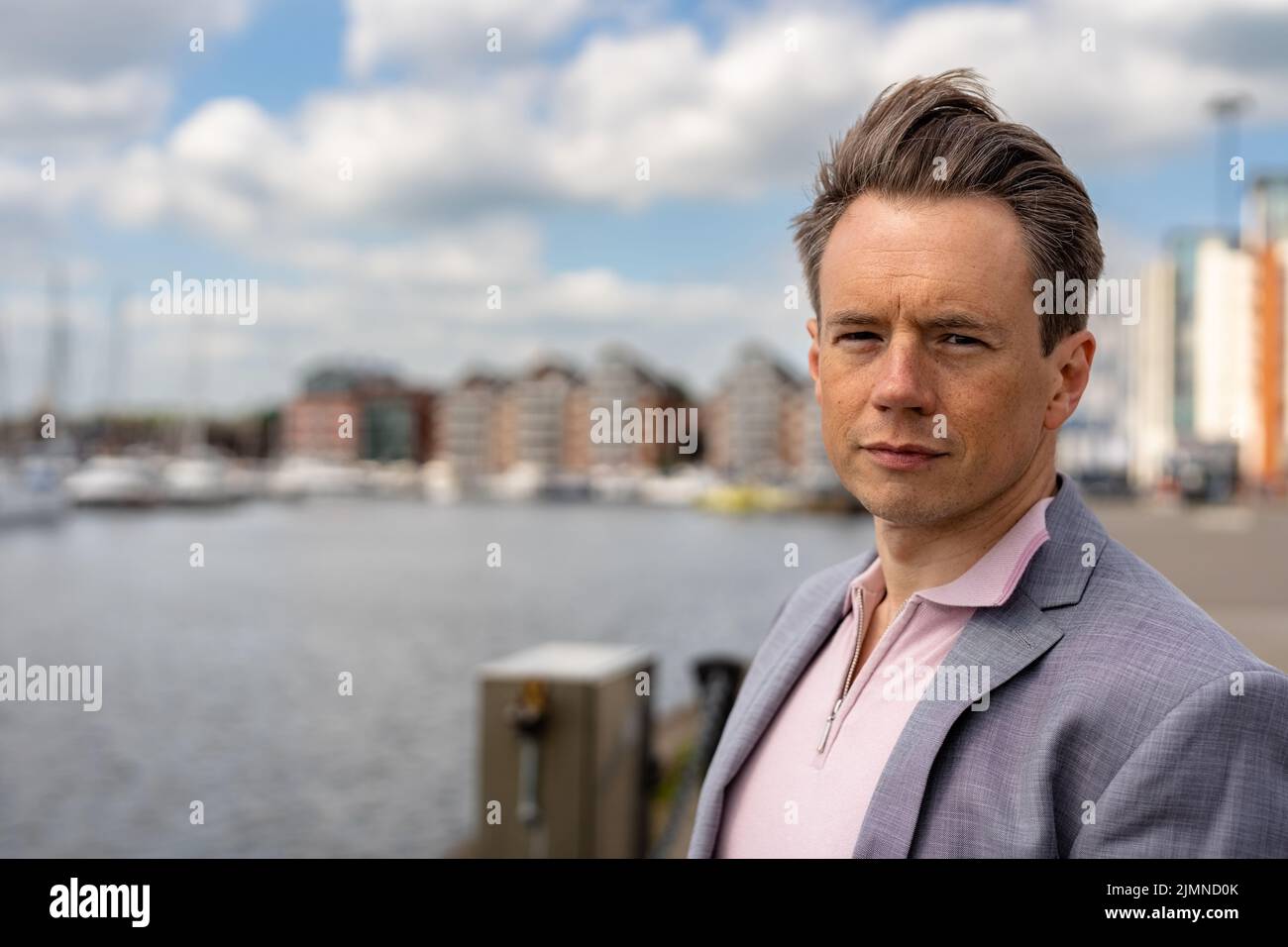 A handsome businessman in a casual grey suit in front of a busy marina with luxury yachts moored up Stock Photo