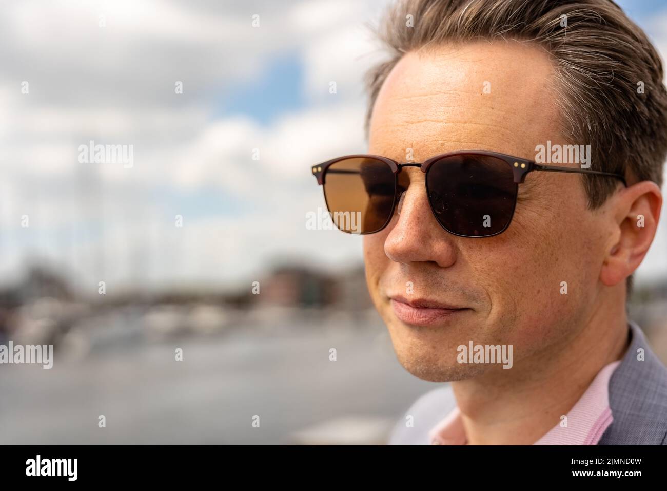 Close up portrait of a handsome businessman in a casual grey suit in front of a busy marina with luxury yachts moored up Stock Photo