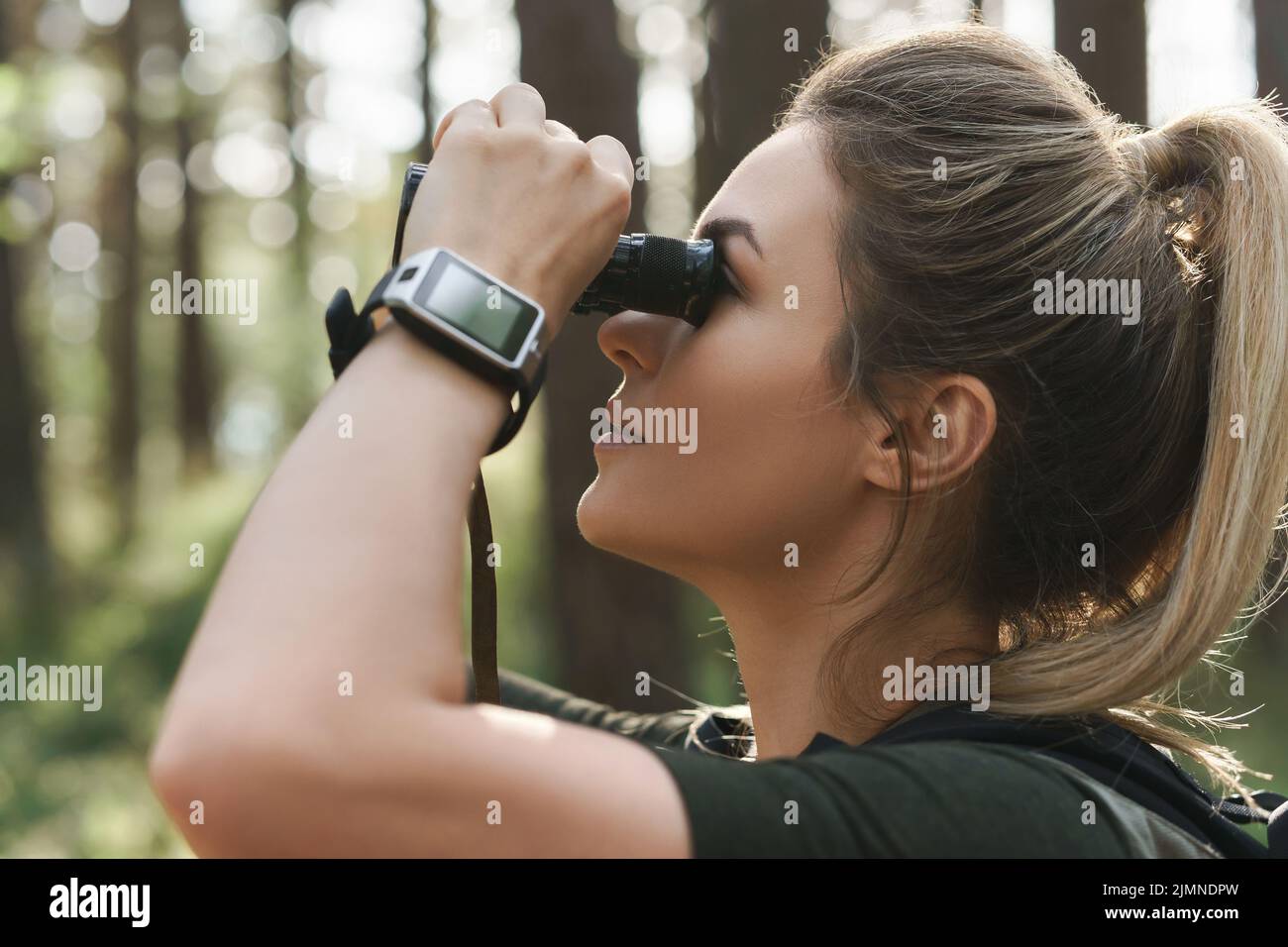 Female hiker is using binoculars for bird watching in green forest Stock Photo