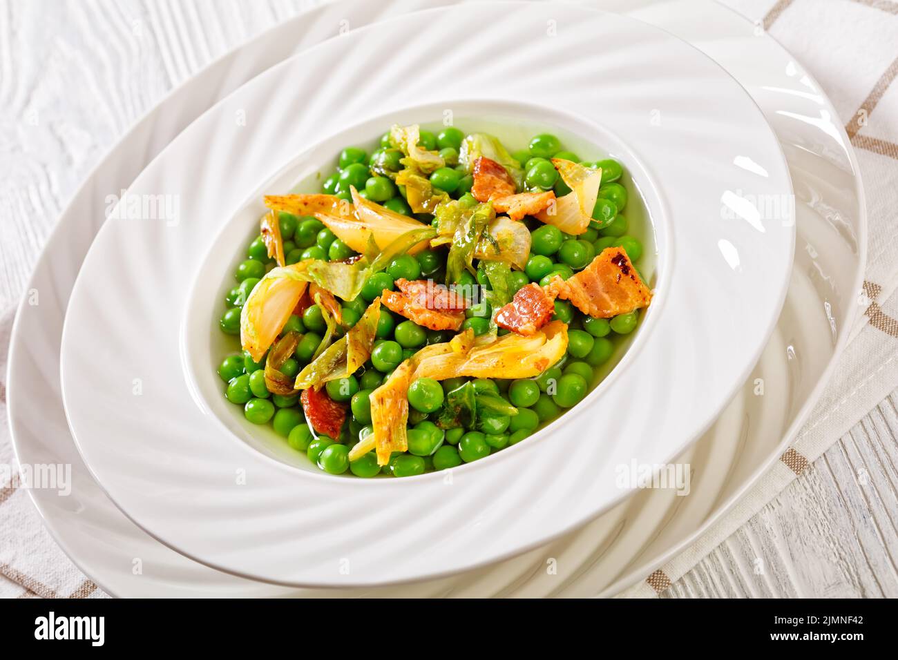 petits pois, french dish of tender, new-season peas braised in chicken stock with lettuce, onion bulbs and speck, cut into lardons, served in white bo Stock Photo