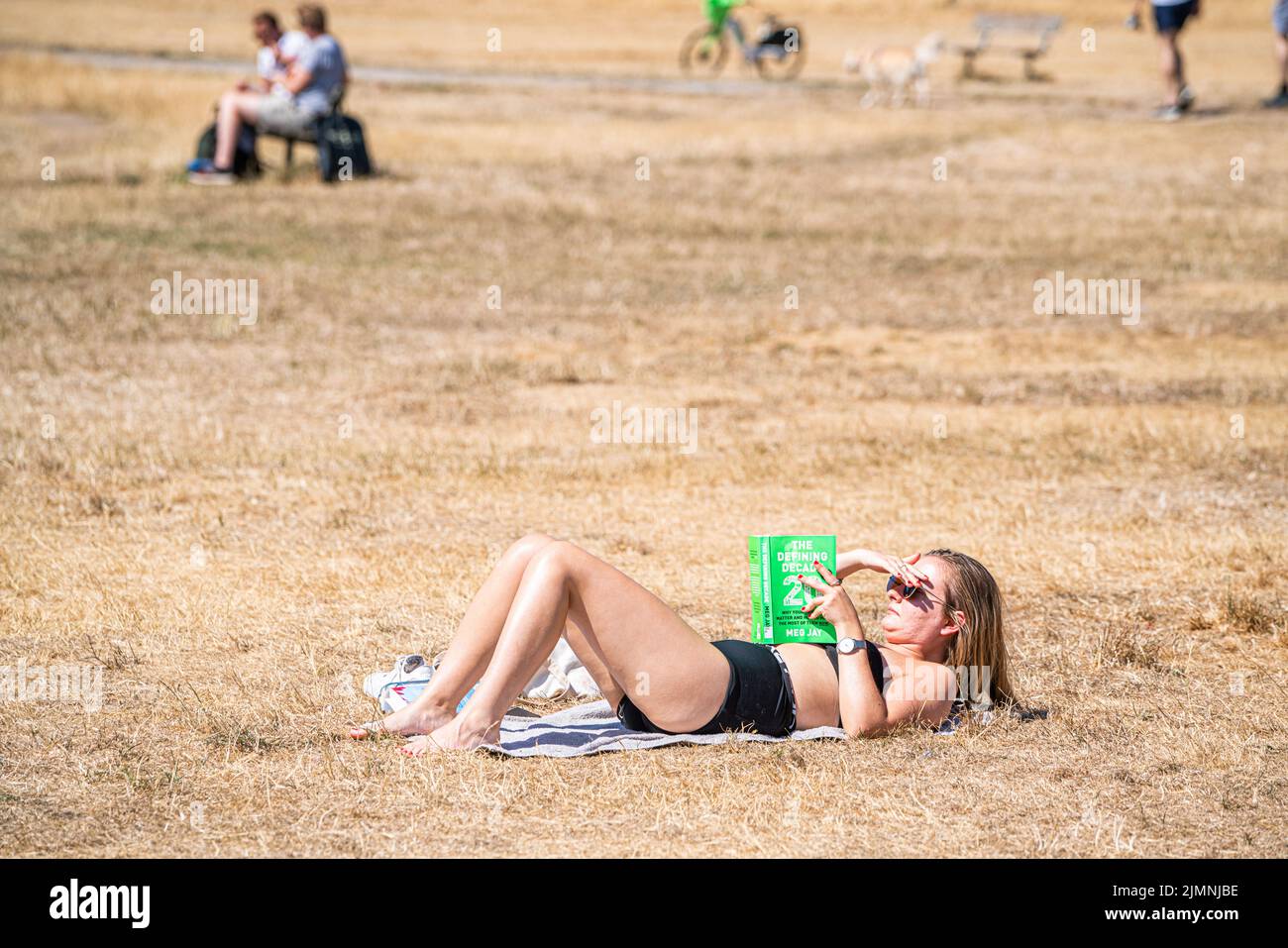 Wimbledon, London, UK. 7 August 2022  A woman  sunbathing on a hot day  on the parched grass on Wimbledon Common  on another  hot day  as the UK's heatwave and drought continues into August, with temperatures expected to reach  above 30celsius  by next week Credit. amer ghazzal/Alamy Live News Stock Photo