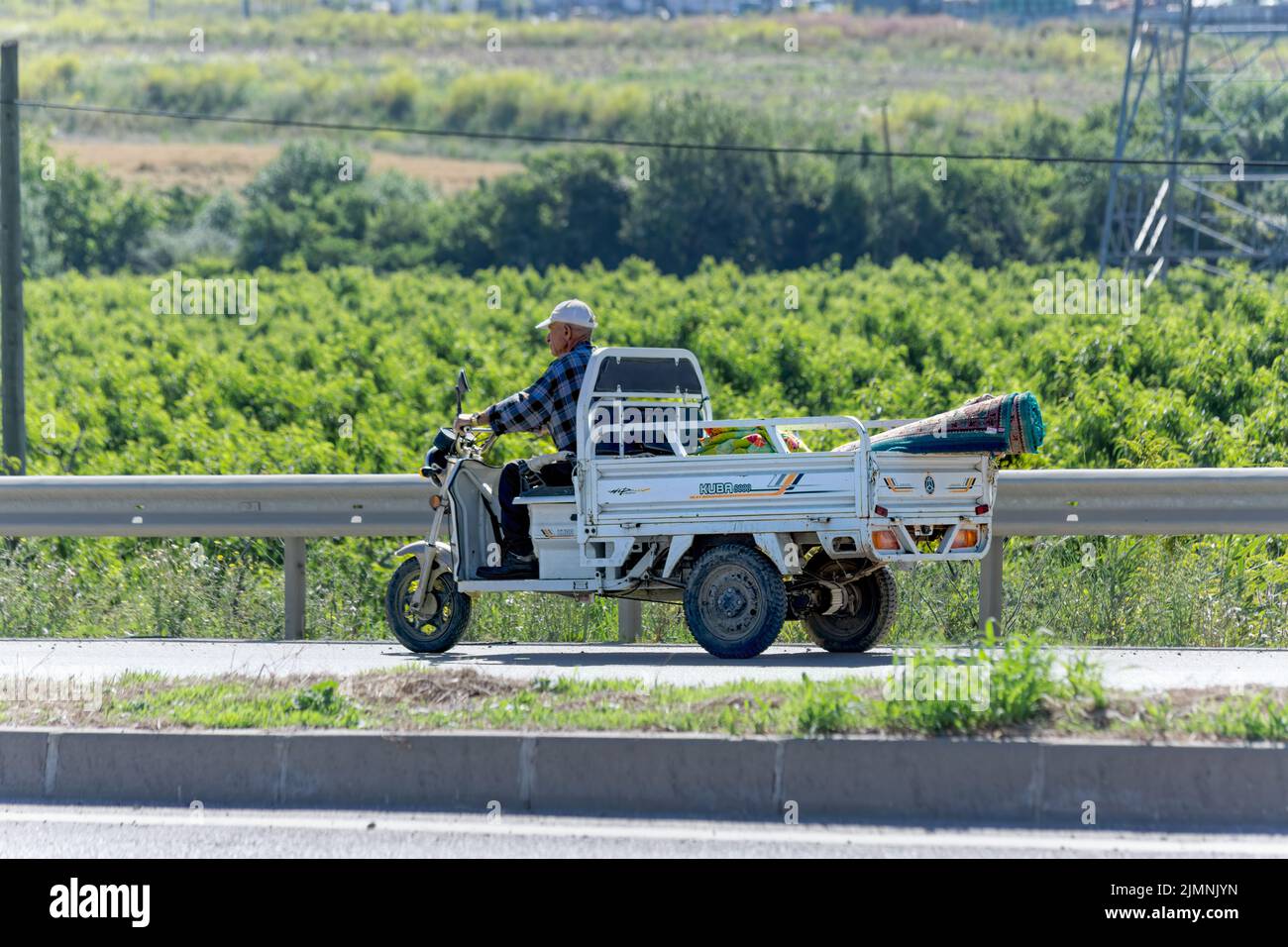 Old man carry carpet with three wheel electric pickup truck on the highway. Stock Photo