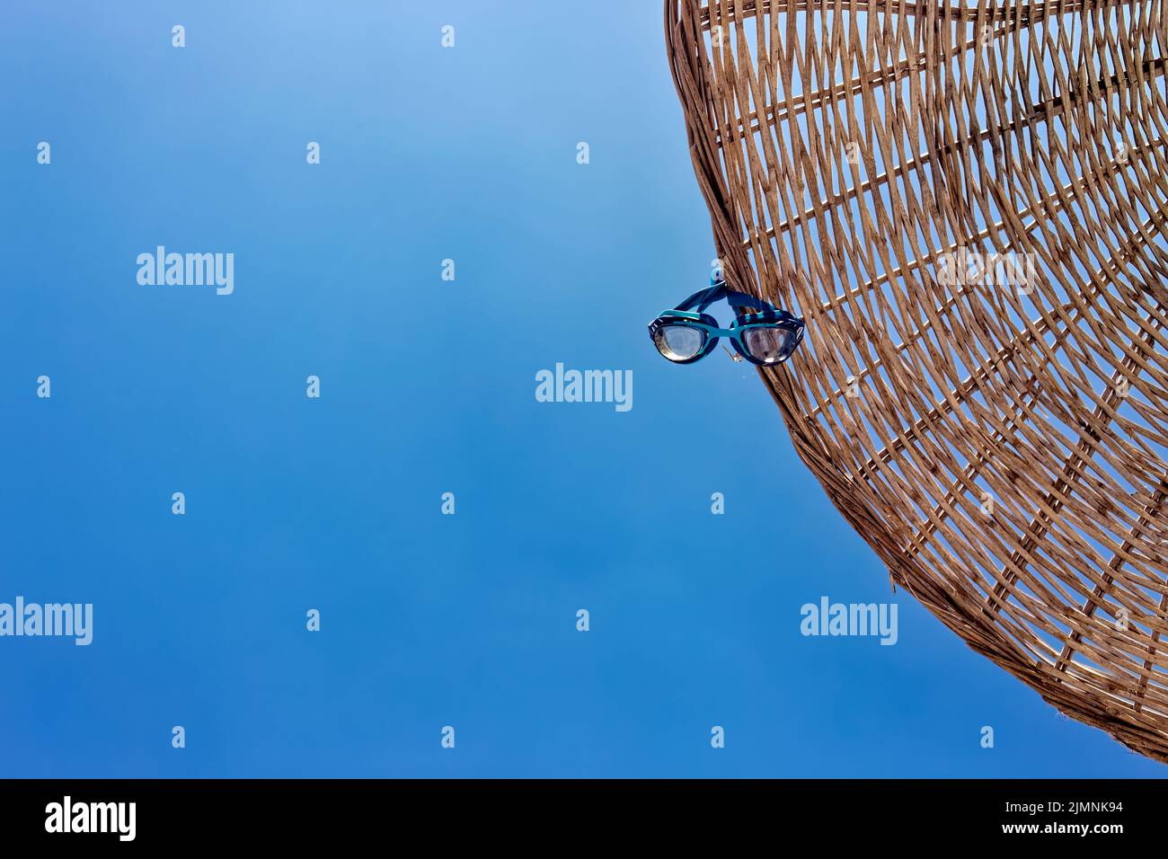 Swim goggles hanging on a parasol umbrella. View from directly below with copy space. Clear, sunny, open sky. Stock Photo