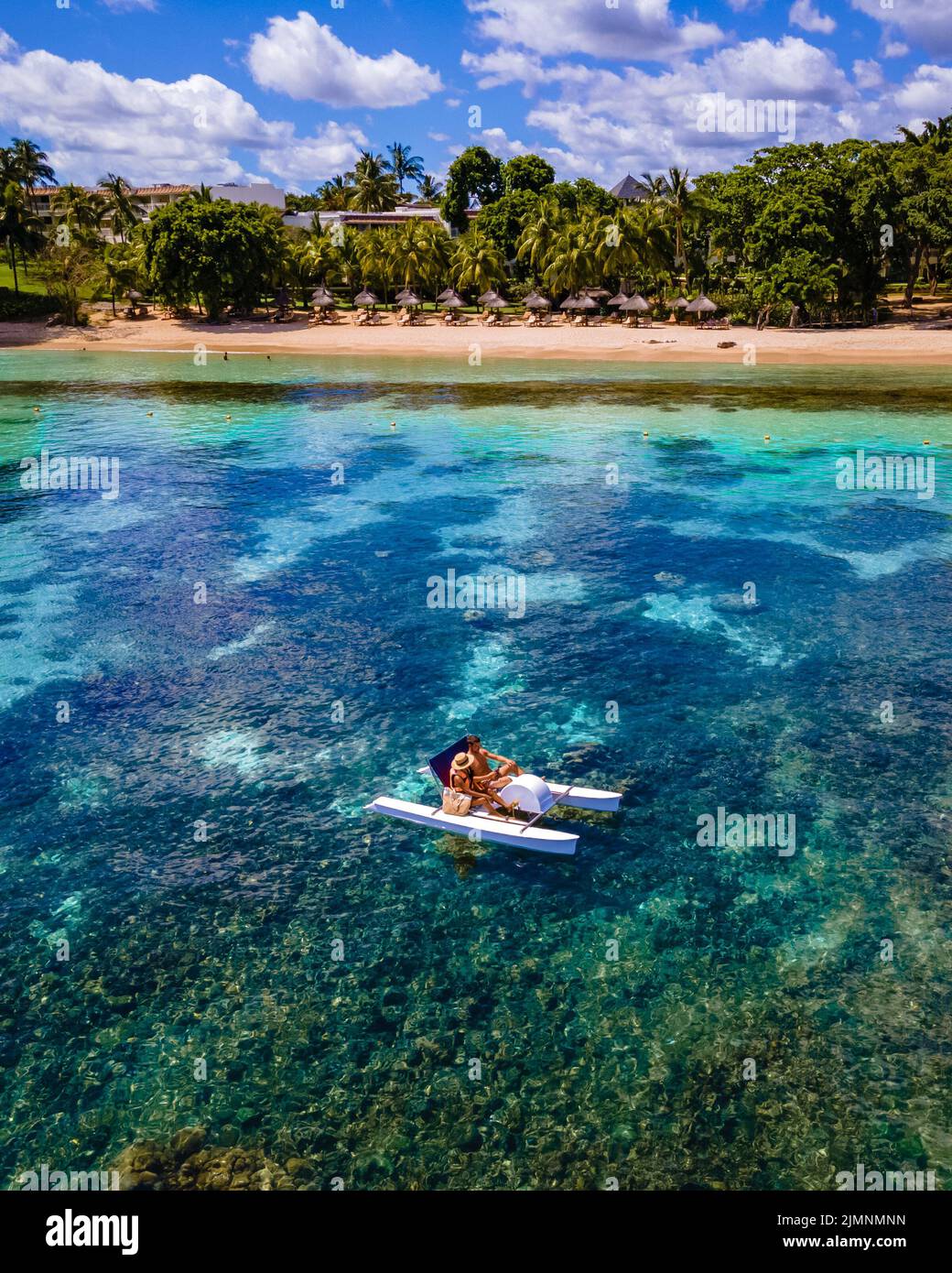 Paddle boards and pedalos on the idyllic palm fringed beach, couple men and woman on vacation Mauritius Stock Photo