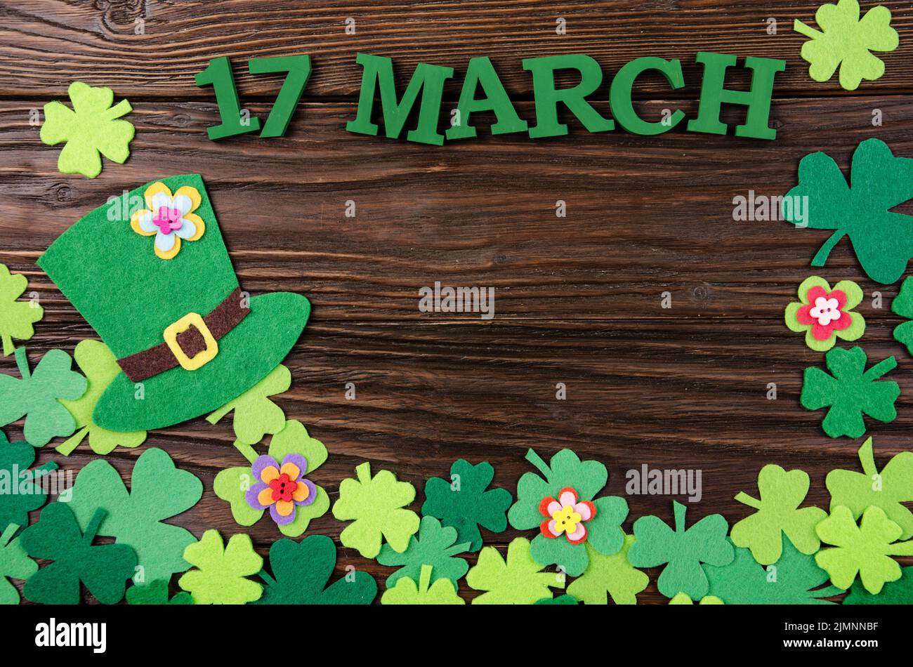 Happy Saint Patrick's mockup of handmade felt hat flowers and shamrock clover leaves on wooden background. Stock Photo