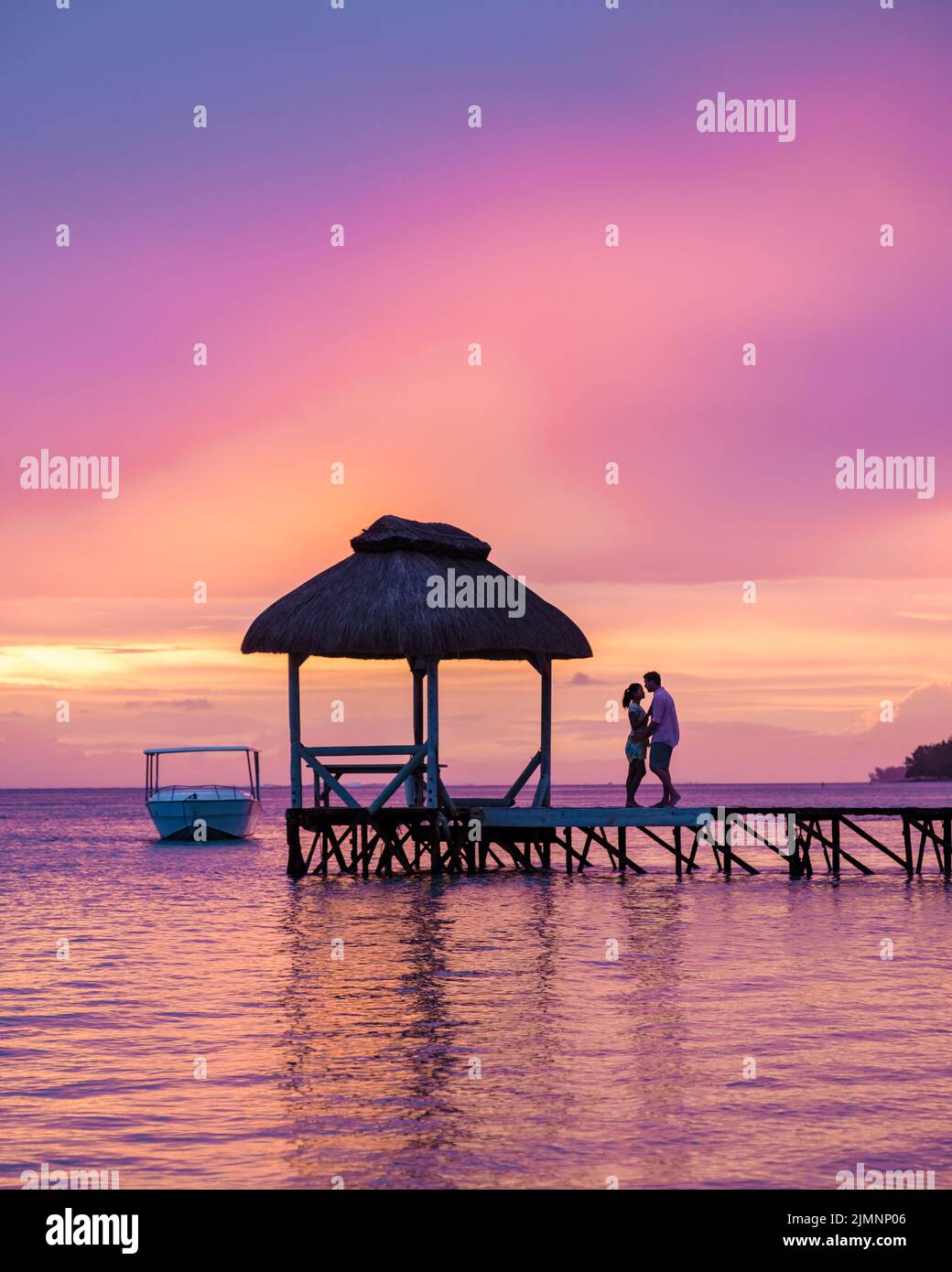 Couple watching sunset on a tropical beach with wooden pier in the ...