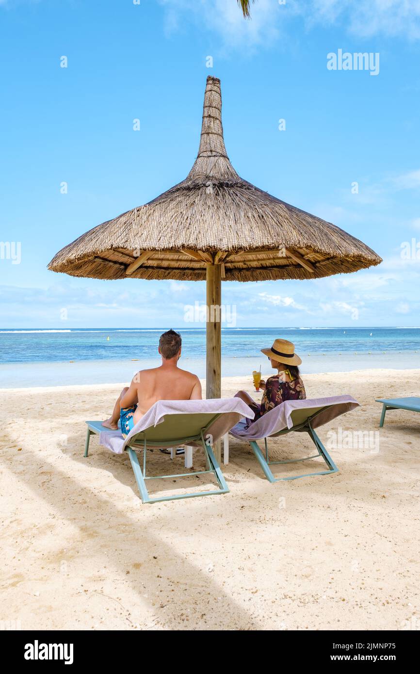 Honeymoon couple sitting in luxury recliners at a tropical Caribbean beach resort and celebrating with a coctail Stock Photo