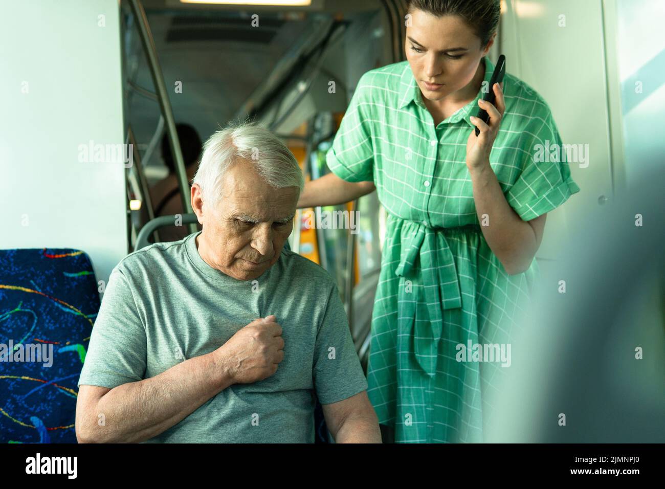 Woman calling to emergency line because elderly man having heart attack symptoms in public transport Stock Photo