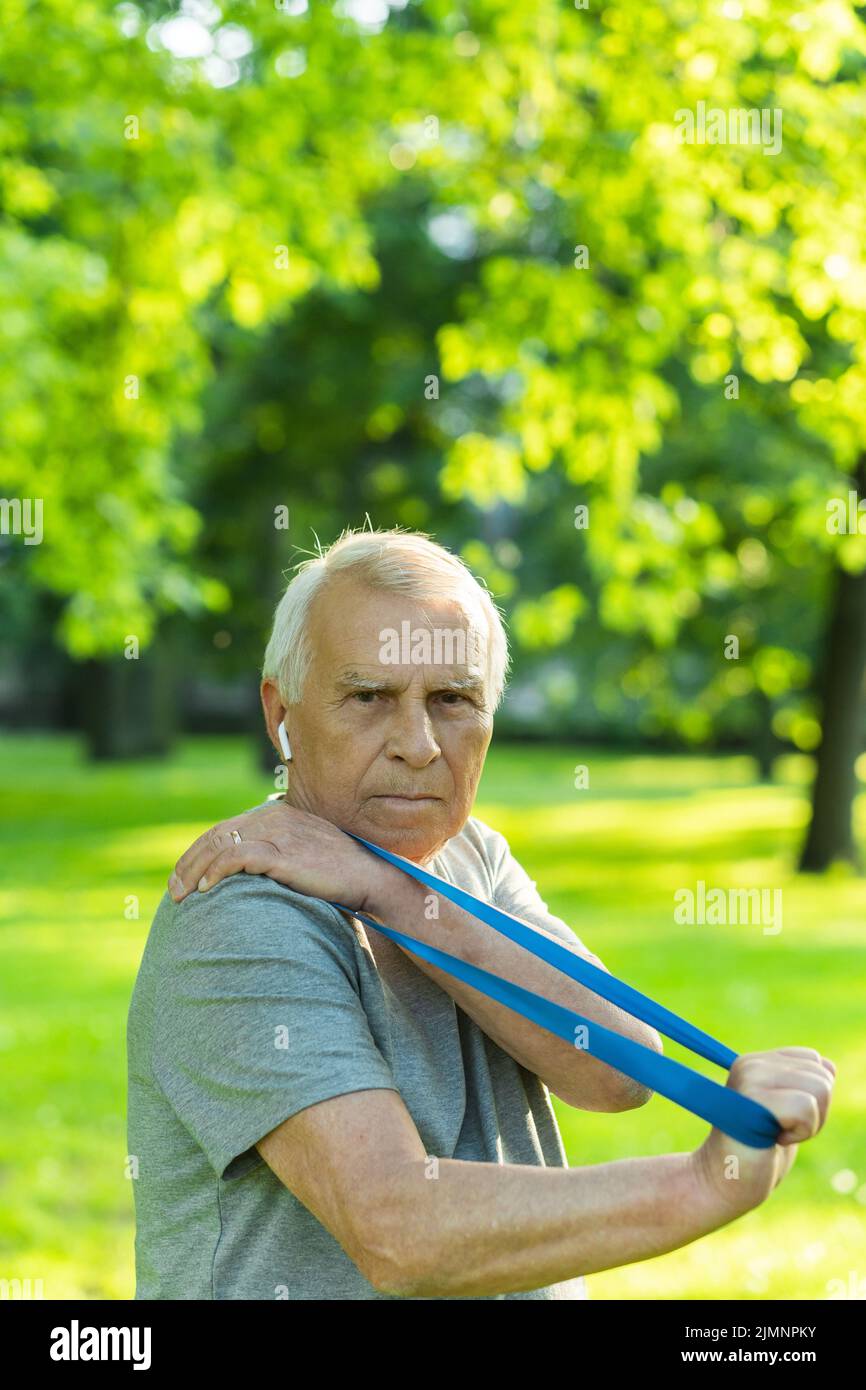 Active elderly man exercising with a rubber resistance band in green city park Stock Photo