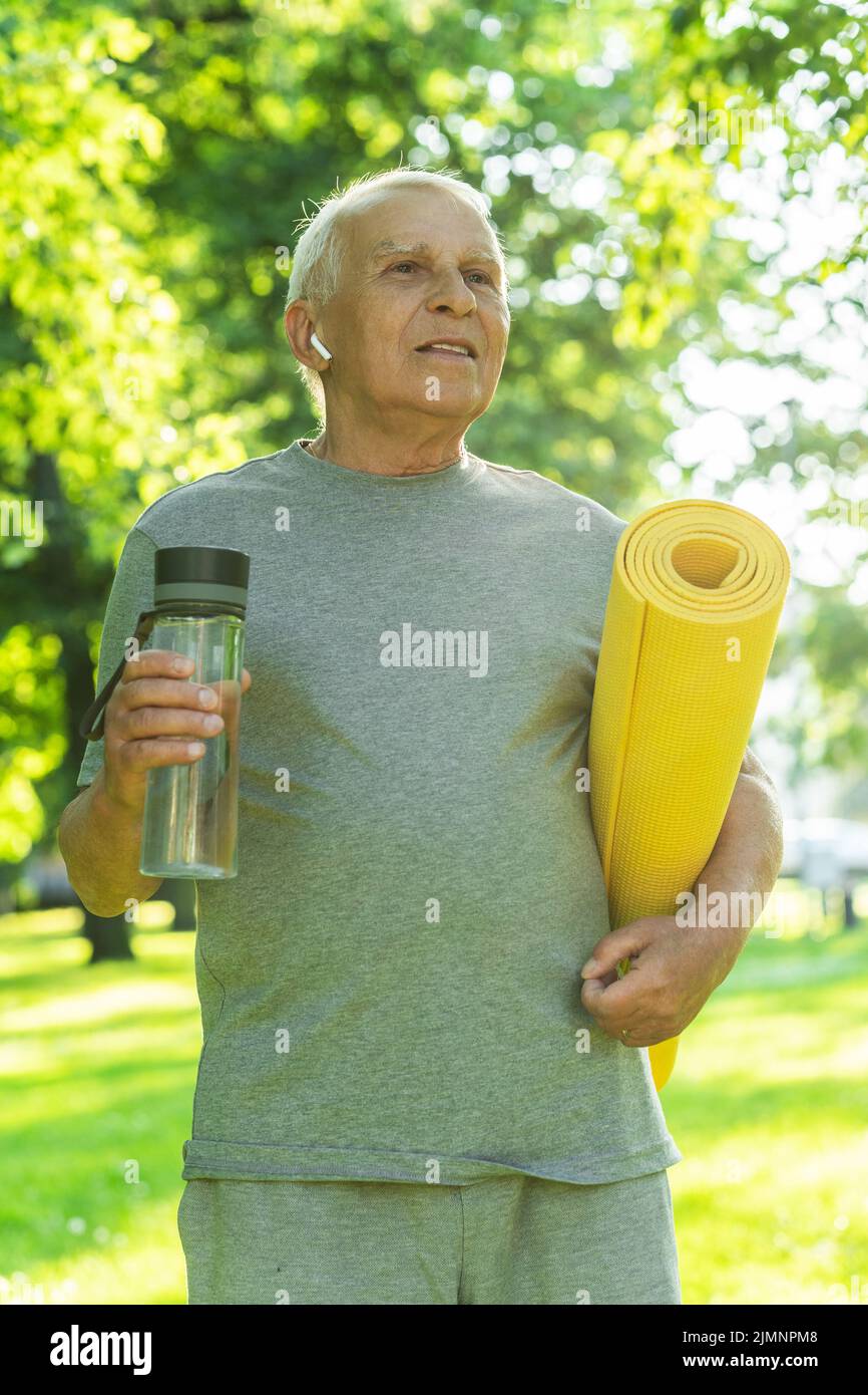 Active elderly man with a exercise mat and bottle of water in green
