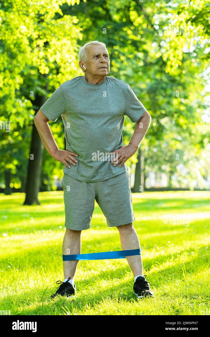 Active elderly man exercising with a rubber resistance band in green city park Stock Photo