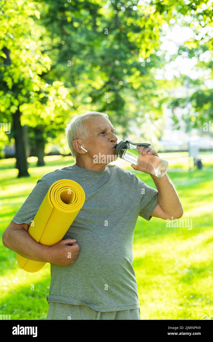 Active elderly man with a exercise mat and bottle of water in green ...