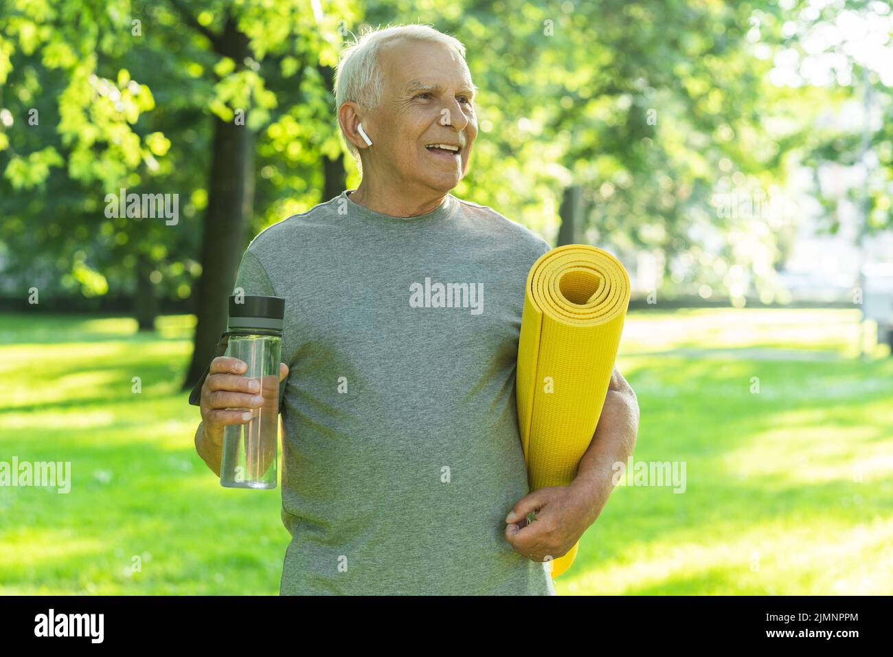 Active elderly man with a exercise mat and bottle of water in green ...