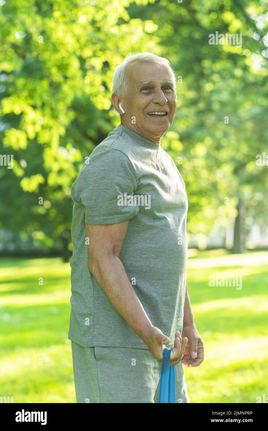 Active elderly man exercising with a rubber resistance band in green city park Stock Photo