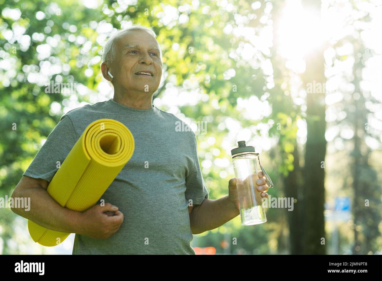 Active elderly man with a exercise mat and bottle of water in green ...