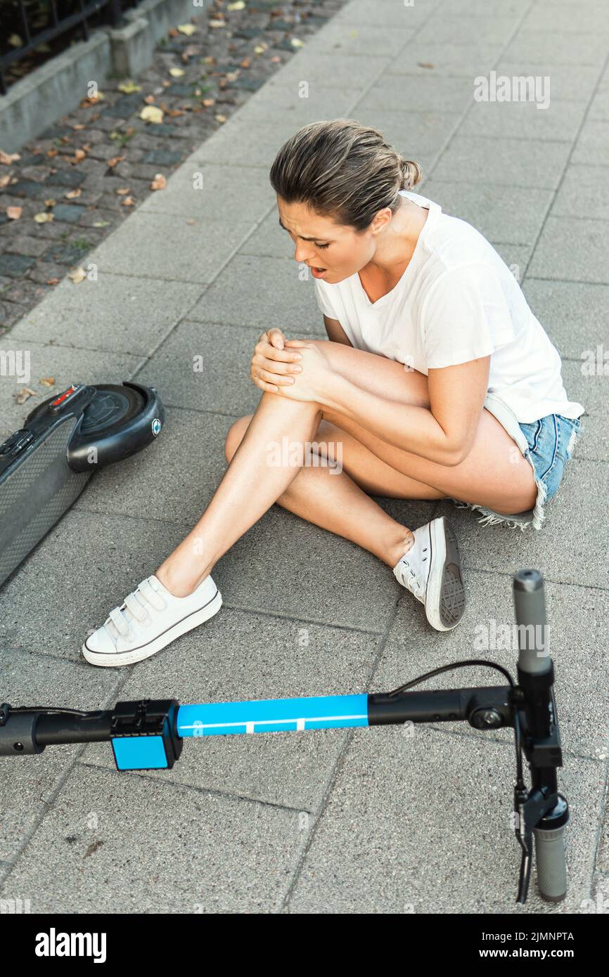 Young woman suffering from knee pain after e-scooter riding accident Stock Photo