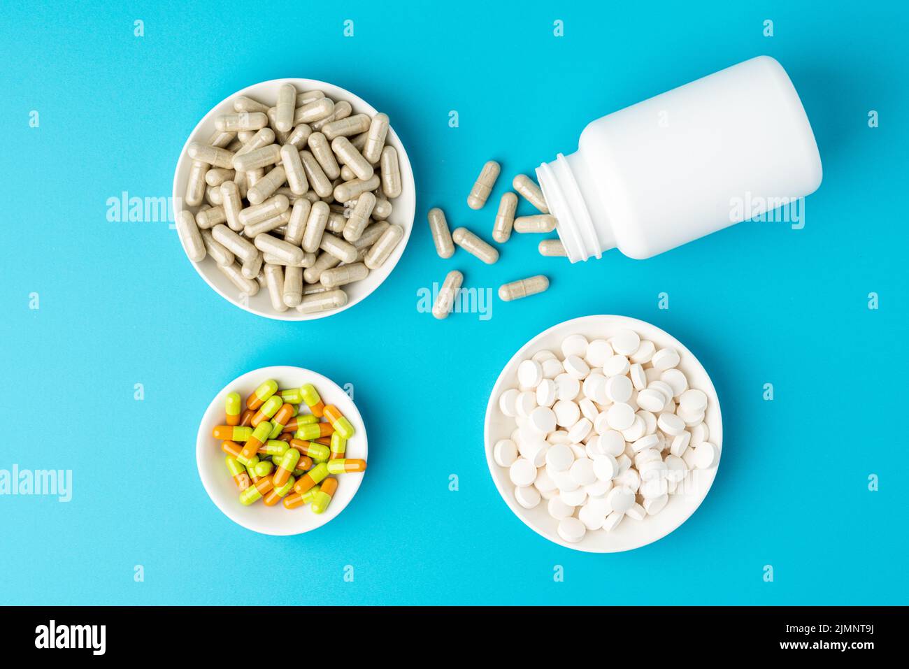 Blue background of large group of assorted capsules, pills and tablets in bottle and bowl Stock Photo
