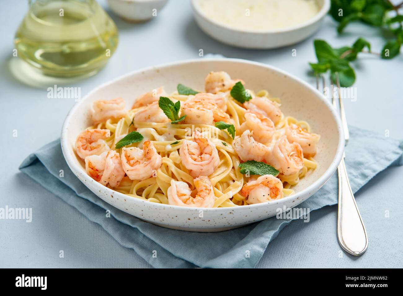Pasta spaghetti with fried shrimps, bechamel sauce, mint leaf on blue table Stock Photo
