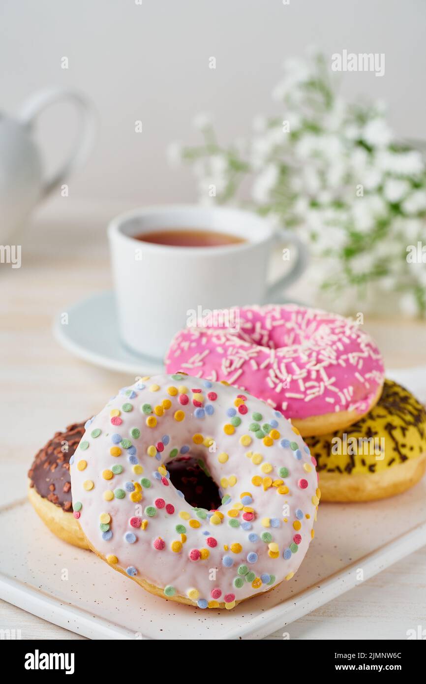 Doughnuts and tea. Bright, colorful junk food. Vertical. Light beige wooden background Stock Photo