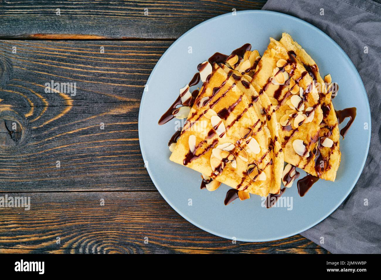 Two pancakes with chocolate syrup, almond flakes on plate, honey flows from spoon Stock Photo