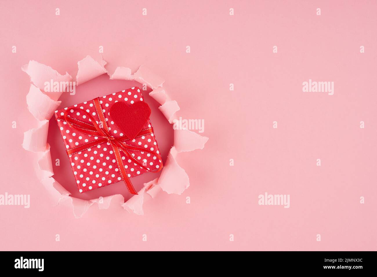 Valentine's Day. A ripped hole and red heart with gift box in bright pink Stock Photo