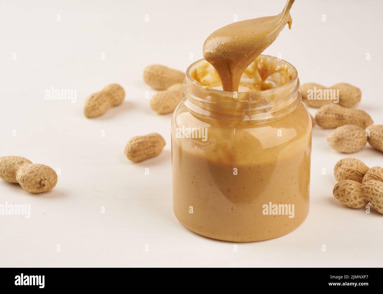 Jar of peanut butter and peanuts in shell on a white table, side view, fresh ground crushed nuts, side view Stock Photo