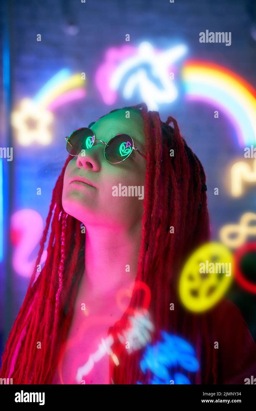 Girl in neon lights, beautiful woman in sunglasses, with pink hair, with dreadlocks pigtails Stock Photo