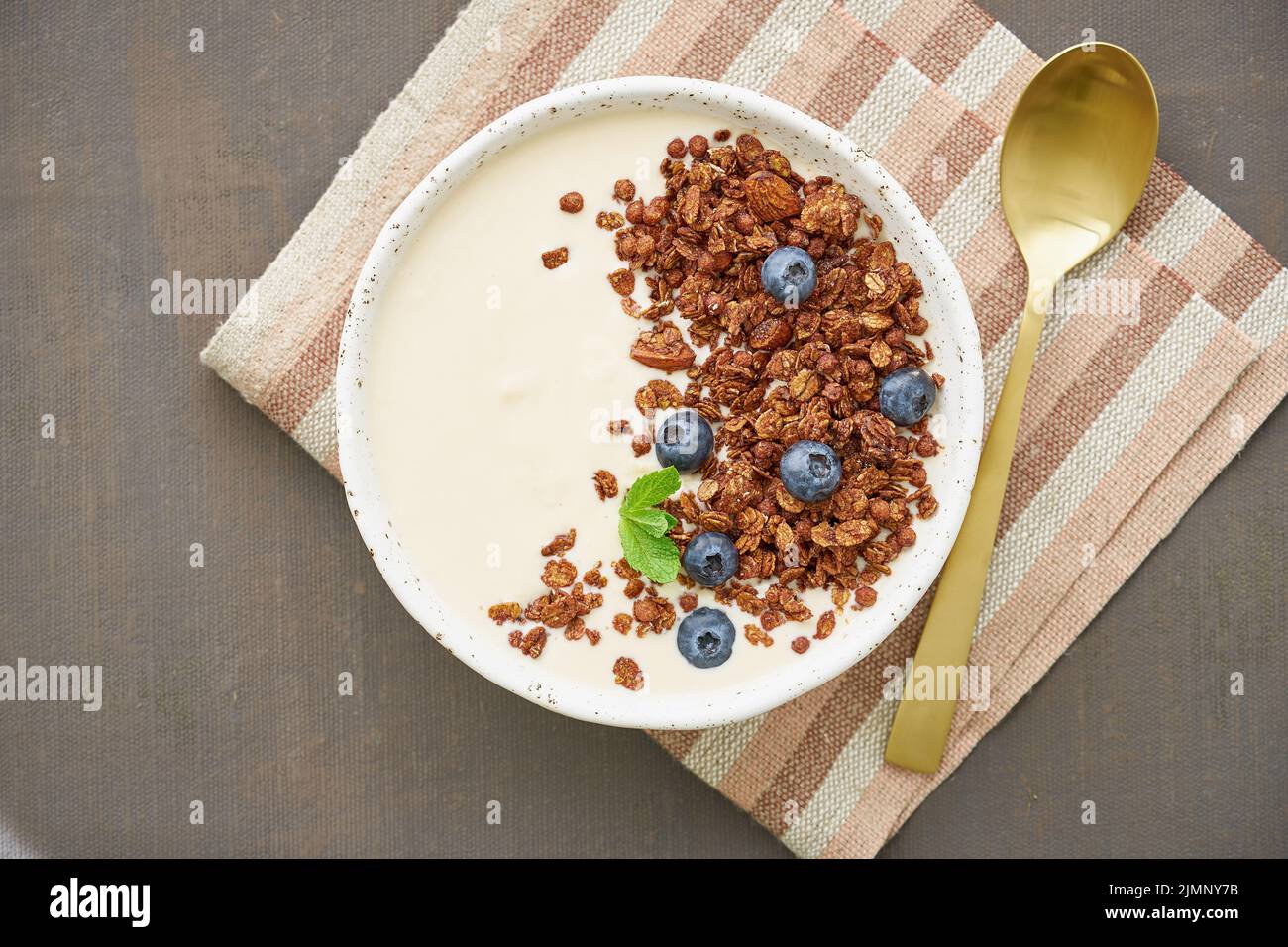 Yogurt with chocolate granola, bilberry. Breakfast on a brown table, top view Stock Photo