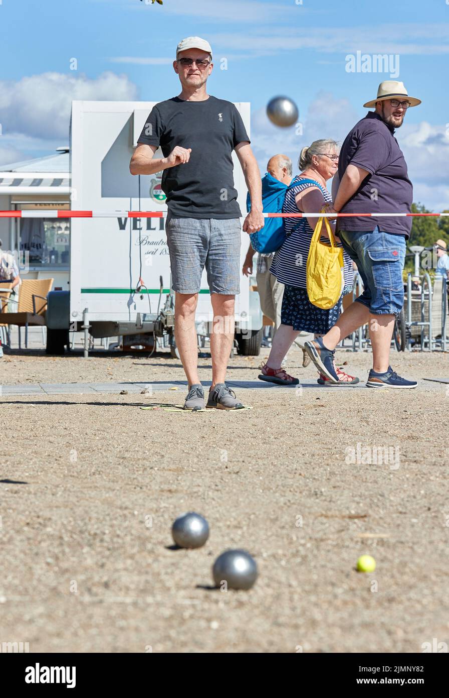 07 August 2022, Schleswig-Holstein, Lübeck: Sönke Backens (l), women's coach from Freiburg, throws a ball on the beach promenade. The Holstentor tournament is considered the largest German boules tournament. Photo: Georg Wendt/dpa Stock Photo