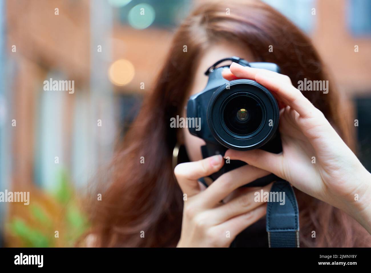 Beautiful stylish fashionable girl holds a camera in her hands and takes pictures. Woman photographer with long dark hair Stock Photo